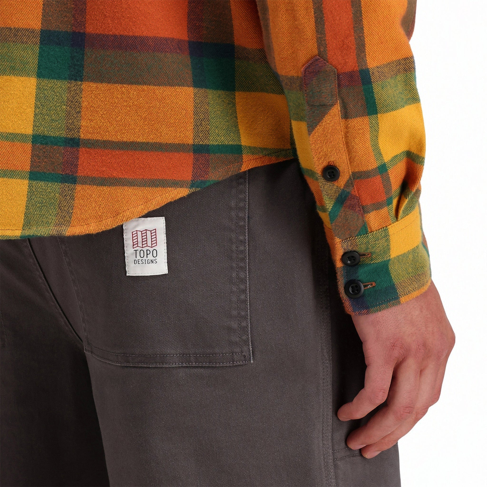 Back model shot of Topo Designs men's mountain organic cotton flannel shirt in "brick / mustard plaid" orange showing cuff details