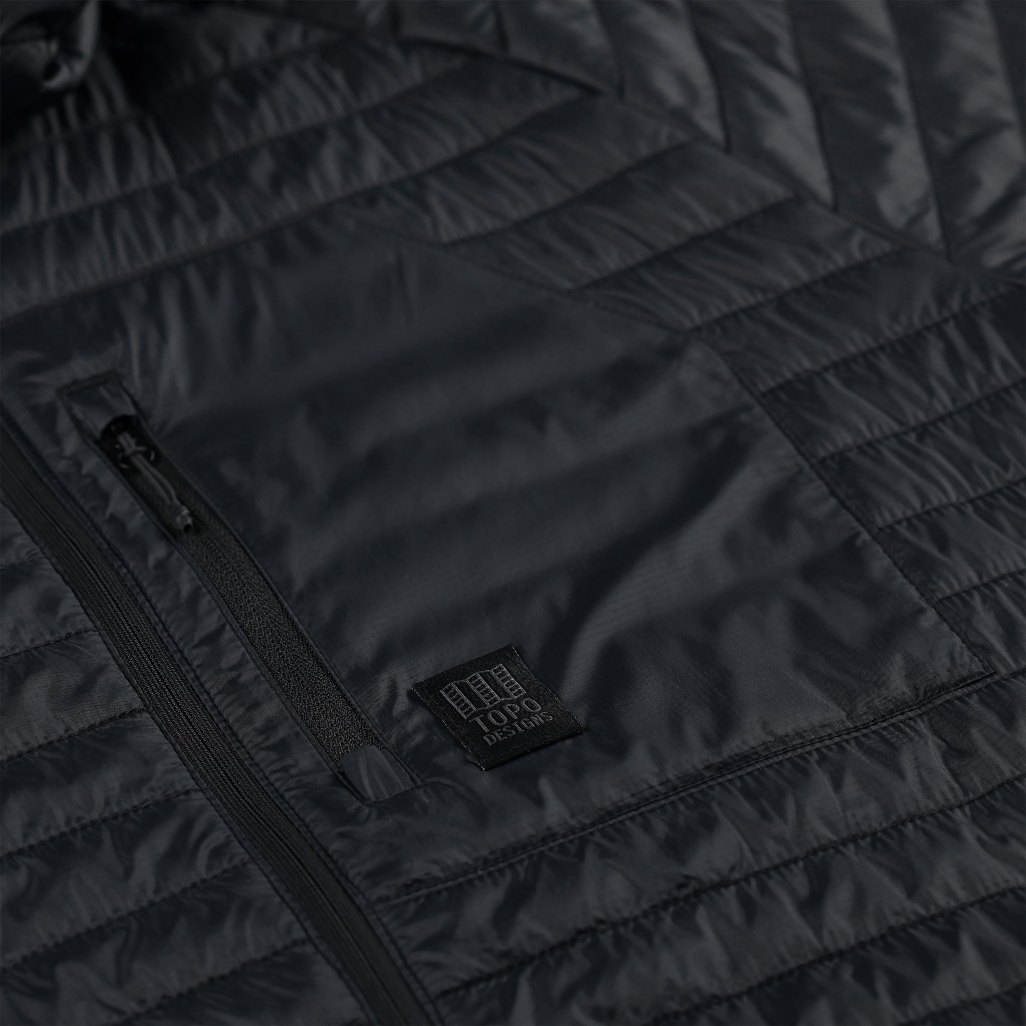 General detail shot of zipper chest pocket on Topo Designs Women's Global Puffer recycled insulated packable Hoodie jacket in "black"