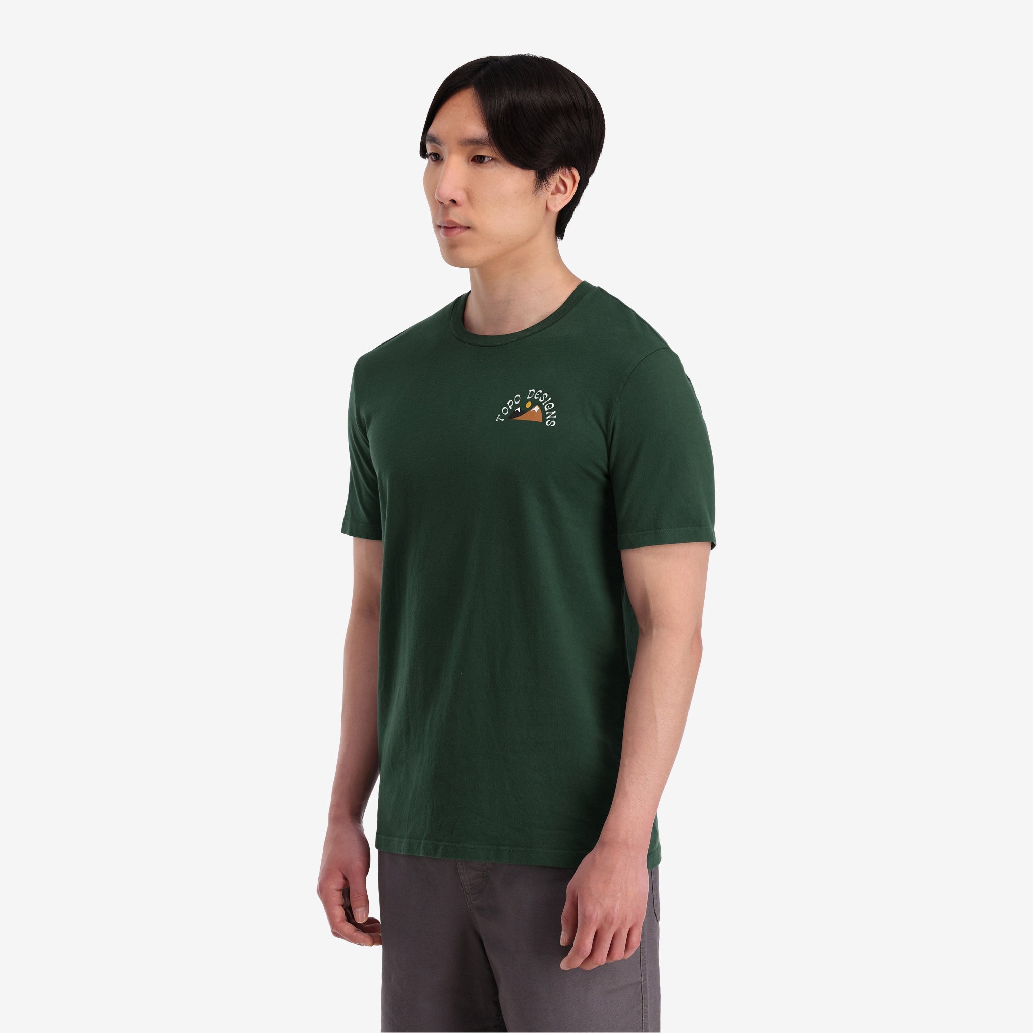 General shot on model side view of Topo Designs Men's Alpenglow Tee 100% organic cotton graphic short sleeve t-shirt in "forest" green.